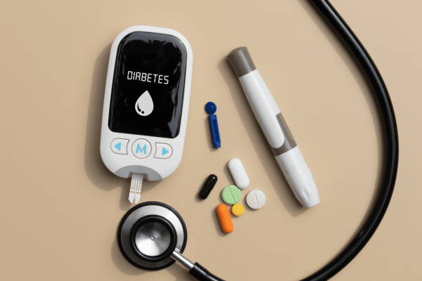 Diabetes testing kit with glucometer, pills, and stethoscope on a beige surface.
