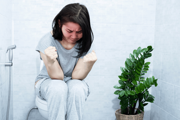 Woman sitting on a toilet, appearing to strain or feel discomfort.