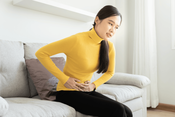 Woman sitting on a couch holding her abdomen in discomfort or pain.