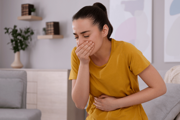 Woman in a yellow shirt covering her mouth and holding her stomach in discomfort.