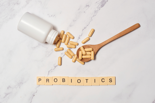 Capsules spilled from a bottle and a wooden spoon with tiles spelling ‘PROBIOTICS’.