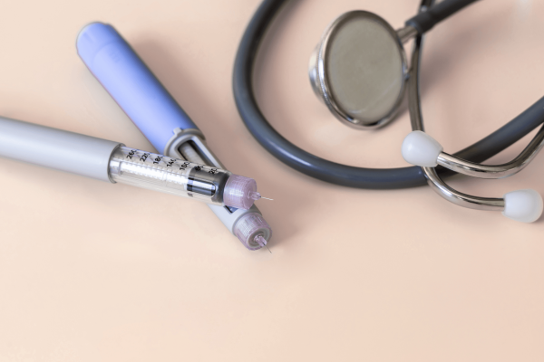 Close-up of insulin pens and a stethoscope on a light-colored surface.
