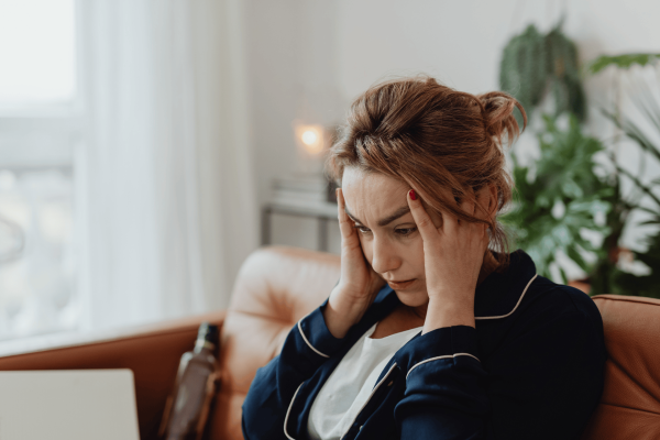 Woman sitting on a couch holding her head in pain, appearing to have a headache.