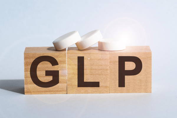 Wooden blocks spelling GLP with white tablets placed on top.