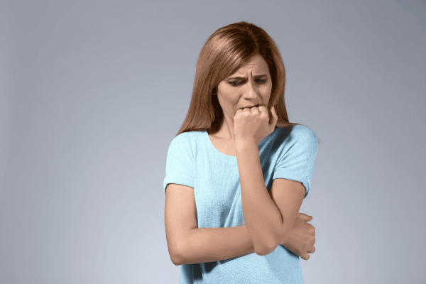 Woman in blue shirt biting her fist, looking anxious.
