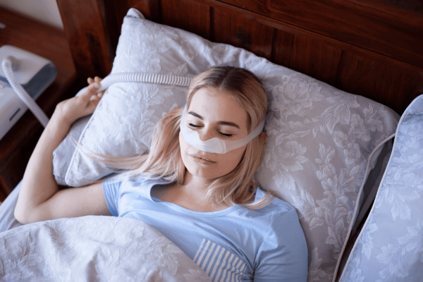 Woman sleeping in bed wearing a CPAP nasal mask to treat sleep apnea
